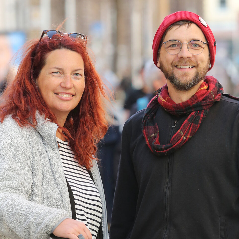2 Menschen stehen nebeneinander in einer Fußgängerzone. Sie schauen freundlich in die Kamera.