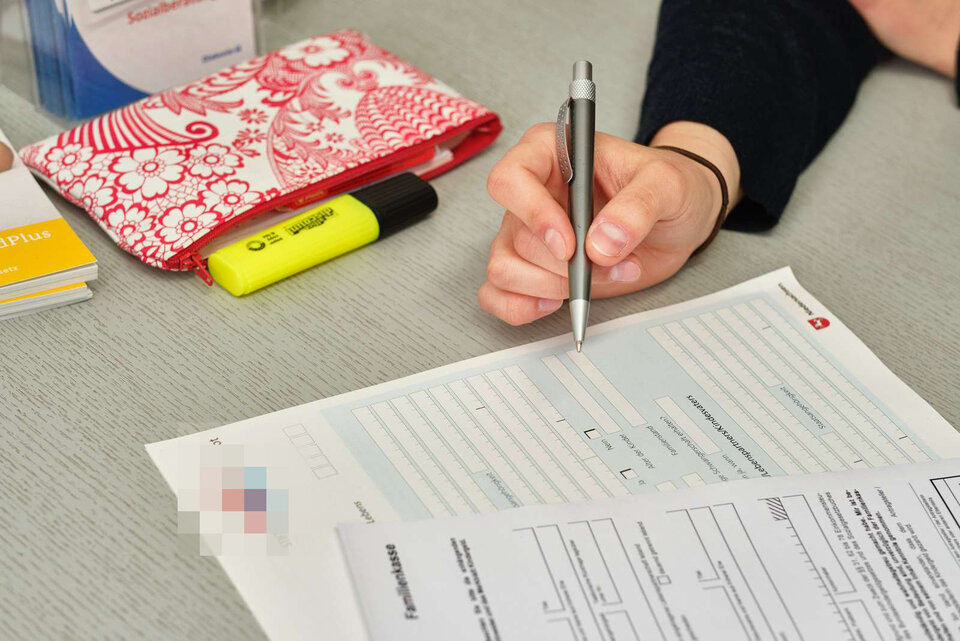 Formulare liegen auf einem Tisch, man sieht eine Hand mit einem Kugelschreiber über den Formularen.