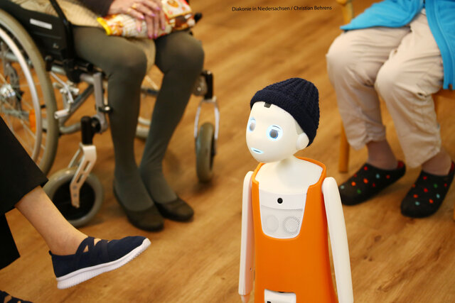 Der Roboter Navel steht zwischen sitzenden Menschen in einem Altenheim