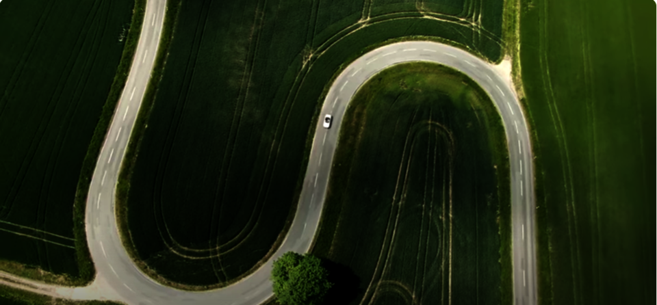 Eine Straße im Grünen von oben. Auf der Straße fährt ein Auto.