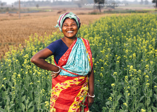 Indigene Kleinbäuerin in Bangladesch. Sie steht in einem Feld und lacht 