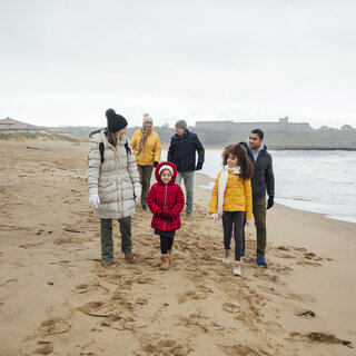 Eine Familie läuft an einem Strand auf die Kamera zu, es ist kalt, sie tragen Winterkleidung.