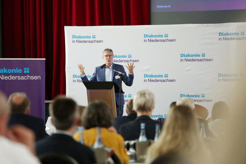 Thomas Hofer auf der Bühne der Mitgliederversammlung, im Vordergrund sieht man Teile des Plenums von hinten