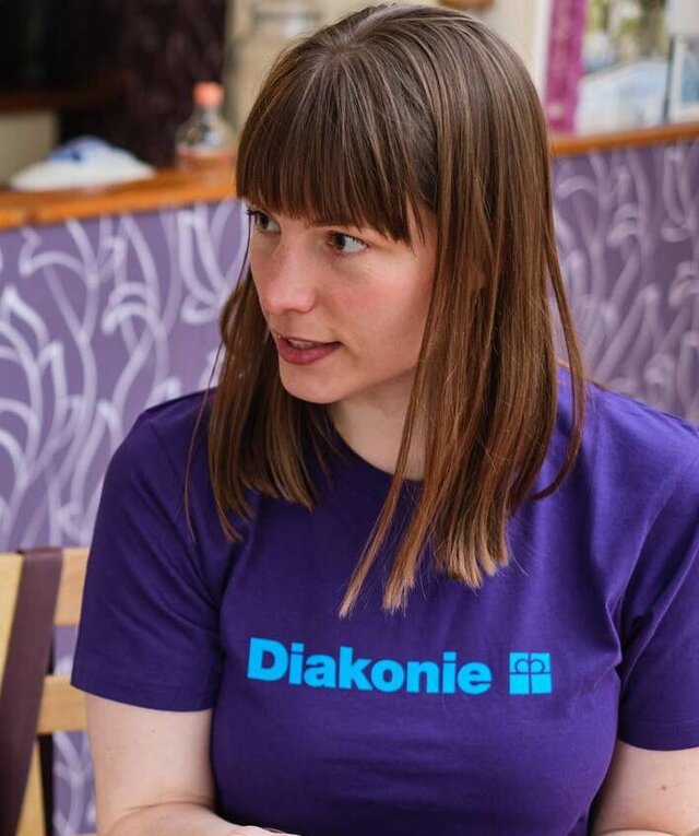 Eine Frau, die ein T-Shirt mit der Aufschrift "Diakonie" trägt, berät eine andere Person. Die andere Person ist nicht im Bild.